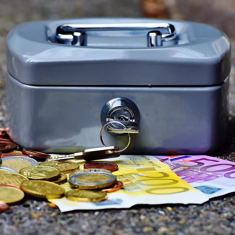 Caja de dinero con una llave en su cerradura, rodeada de monedas